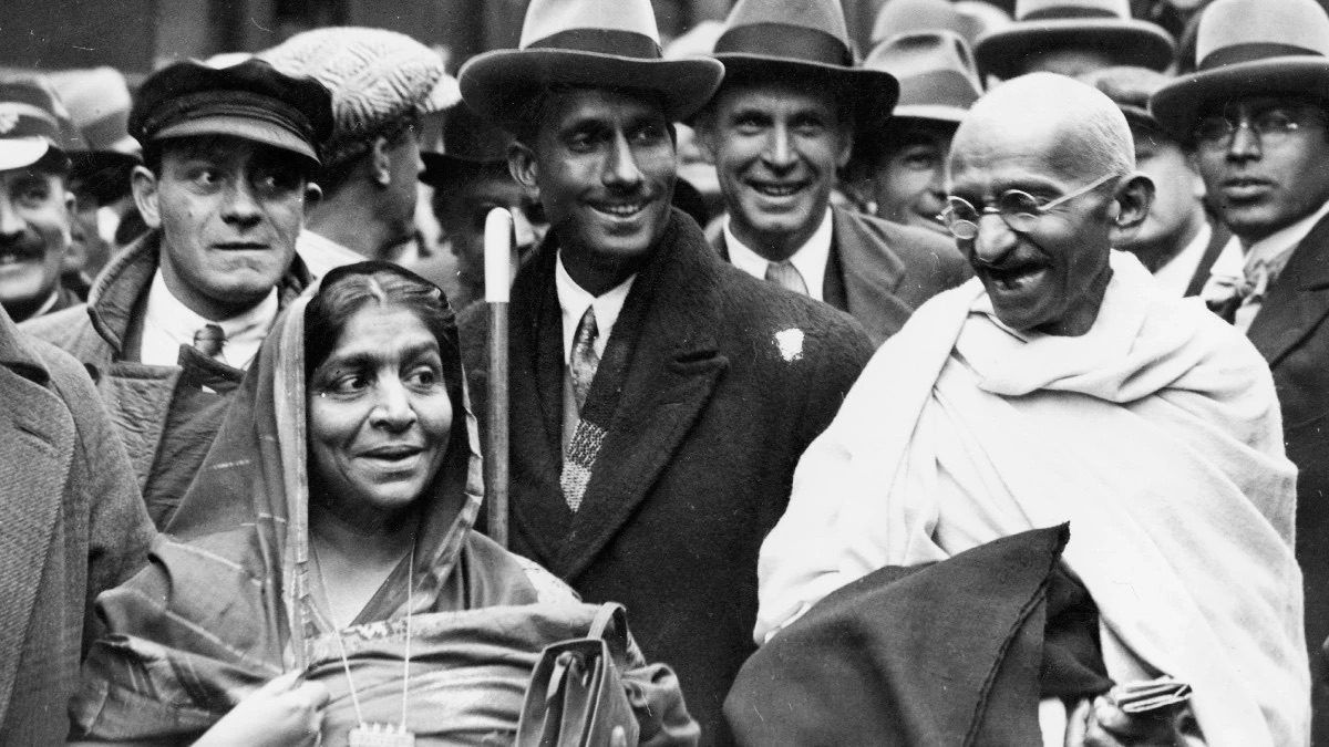 Sarojini Naidu and Mahatma Gandhi in a crowded London street, surrounded by men in overcoats and hats.